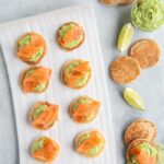 gluten-free blini topped with avocado cream and smoked salmon, served with lime wedges and avocado cream on the side