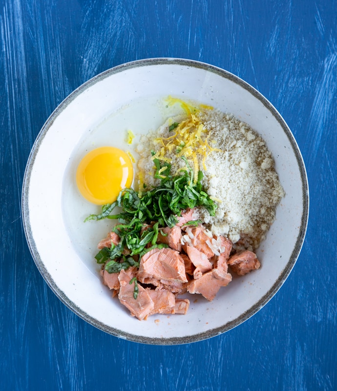 cooked salmon, lemon zest, egg, chopped basil leaves and almond flour in a white bowl.